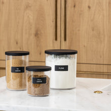 Load image into Gallery viewer, grouping of clear canisters with black lids organizing baking supplies