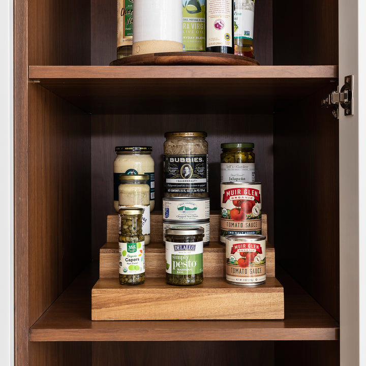 acacia wood expandable riser in kitchen cabinet holding canned goods