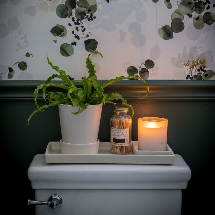 bathroom counter with white ceramic trays holding a candle, matches and a plant