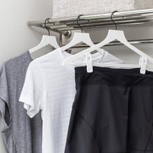 Load image into Gallery viewer, white slim, non-slip suit hangers with white hanger clips holding athletic wear in a laundry room
