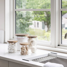 Load image into Gallery viewer, laundry room with glass jars with acacia wood lids holding laundry supplies like detergent, dryer balls and clothes pins
