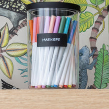 Load image into Gallery viewer, clear canister with black lid holding markers on playroom shelf
