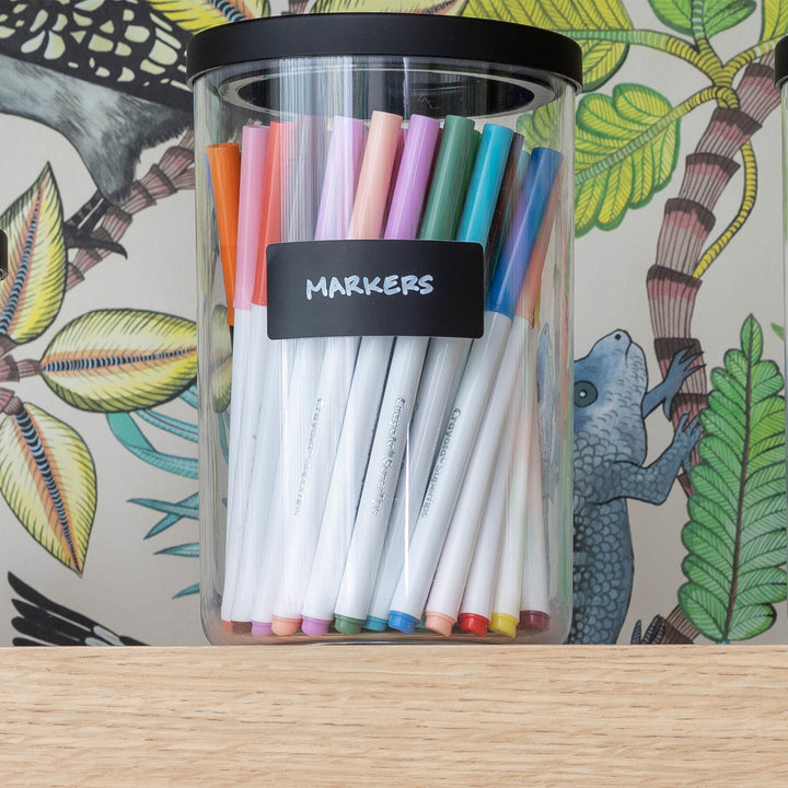 clear canister with black lid holding markers on playroom shelf