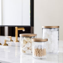 Load image into Gallery viewer, clear canisters with gold lids organizing bathroom items like cotton balls, q-tips and face sponges 
