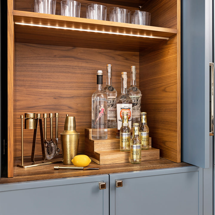 acacia wood expandable riser in cabinet holding bottled liquor
